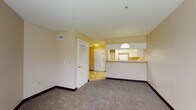 This single-floor unit is thoughtfully laid out to maximize functionality and comfort. The open-concept living area is finished with wall-to-wall carpet and neutral, warm-toned walls, creating a welcoming atmosphere. A raised breakfast bar visually separates the living space from the kitchen, which is illuminated by a pendant light overhead. The kitchen is outfitted with white cabinetry providing generous storage, light-toned countertops, a full-size refrigerator, and an electric range with an overhead ventilation hood. Tile flooring runs throughout the kitchen and entry areas, offering a practical contrast to the carpeted living and sleeping spaces.

The unit includes spacious bedrooms, each carpeted and featuring neutral walls with dark baseboards. One bedroom benefits from a large window that invites natural light and offers a view of greenery outside. Both bedrooms provide access to closet space and connect conveniently to the hallway. The bathroom includes a full soaking tub with a tub surround, a toilet, and a vanity with a white countertop, all set on tile flooring. Throughout the unit, the overall ambiance is clean, functional, and move-in ready.