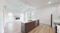 Located at 21 Forest Ridge Blvd in Mechanicville, NY, this single-floor home showcases a clean, modern design with an open and airy layout. The heart of the home is a spacious open-concept living and kitchen area with soaring vaulted ceilings, a ceiling fan, and a sleek electric fireplace. Large windows invite abundant natural light and provide views of the surrounding neighborhood. The kitchen is well-appointed with a large central island featuring dark wood-tone cabinetry and a white quartz countertop, pendant lighting, a stainless steel sink, and a dishwasher. Perimeter cabinetry in crisp white pairs with stainless steel appliances, including a refrigerator, range, and microwave. Light wood-tone flooring runs throughout the main living areas, lending warmth and continuity. The bedrooms are carpeted for comfort, with multiple windows and individual wall-unit HVAC systems. A walk-in closet with built-in shelving provides generous storage. The bathrooms are finished with large-format tile, dual-sink vanities with quartz countertops and contemporary cabinetry, and tiled shower surrounds with brushed nickel fixtures. A dedicated laundry closet with an included washer completes this thoughtfully designed, move-in-ready home.