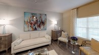 This single-floor residence offers a thoughtfully designed layout encompassing multiple bedrooms, bathrooms, a living and dining area, and a fully equipped kitchen. The living room features warm wood-look flooring, a large statement artwork, and natural light filtering through drape-framed windows, creating an inviting atmosphere. A seamlessly adjoined dining area provides additional functionality with a glass-top table and elegant seating.

The kitchen is outfitted with white shaker cabinetry, granite-style countertops, stainless steel appliances including a refrigerator and microwave, and a double basin sink beneath a window that brings in natural light. Wood-look flooring continues throughout this space for a cohesive aesthetic.

The bedrooms are carpeted and feature ceiling fans, ample natural light from windows with blinds and drape panels, and generous storage. Each room maintains a neutral color palette with warm tones that contribute to a calm, restful ambiance.

The bathrooms are finished with granite-style vanity countertops, framed mirrors, and soaking tubs with shower combinations accented by floor-length curtains, providing a clean and polished look throughout.