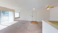 This single-floor residence offers a well-organized layout comprising two bedrooms, two bathrooms, and a versatile den. The open living area is carpeted in neutral tones and receives natural light through a large window with vertical blinds, creating a bright and welcoming atmosphere. A hardwood-floored entryway leads into the main living space, which connects seamlessly to the kitchen via a pass-through counter, making the area feel open and functional.

The kitchen features warm honey-toned wood cabinetry, light countertops, hardwood-style flooring, and white appliances including a refrigerator, range, and dishwasher. Under-cabinet lighting adds practicality to the workspace.

Both bedrooms are carpeted and include ceiling fans with integrated lighting. Each room is served by natural light from windows with blinds. The den provides additional flexible space, also carpeted, ideal for a home office or hobby room.

The two bathrooms are finished with tile flooring, wood-tone vanity cabinetry, and light countertops. One bathroom includes a walk-in shower with glass sliding doors, while the other features a clean, minimalist design with a wide vanity mirror. Overall, the unit maintains a consistent, neutral aesthetic throughout.