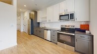 Located at 311 W 22nd St in Kansas City, MO, this efficiently designed one-bedroom, one-bathroom unit offers a well-planned single-floor layout. The open-concept kitchen and living area serves as the heart of the space, featuring light wood-look flooring, recessed lighting, and a large sliding window that floods the room with natural light and provides views of the surrounding cityscape. The kitchen is thoughtfully appointed with two-tone cabinetry — white upper cabinets paired with gray lower drawers — complemented by a classic white subway tile backsplash, dark countertops, and a full suite of stainless steel appliances including a refrigerator, range, microwave, and dishwasher. A hallway connects the main living area to the private bedroom, which is carpeted for comfort and features tall ceilings, a ceiling fan, and a sliding closet. Two closets provide additional storage throughout the unit. The bathroom includes a soaking tub with full subway tile surround and chrome fixtures, maintaining the clean, modern aesthetic found throughout. A dedicated utility room and in-unit laundry add everyday convenience to this smartly designed Kansas City residence.