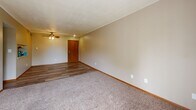 Located at 4320 Westbrook Dr in Ames, Iowa, this one-bedroom, one-bathroom unit offers a practical and well-organized single-floor layout. The living room serves as the heart of the home, featuring a mix of durable wood-look vinyl flooring and plush carpeting, warm neutral-toned walls, and a ceiling fan with light fixture. A sliding glass door fills the space with natural light and provides an outdoor view, enhancing the open feel of the room. The kitchen is efficiently designed with rich dark brown cabinetry, white countertops, a gas range with overhead ventilation hood, and matching wood-look flooring, creating a cohesive and functional cooking space. The bedroom offers comfortable carpeted floors, a ceiling fan, two windows that bring in ample natural light with views of surrounding greenery, and a set of double sliding closet doors providing generous storage. A connecting hallway links the main living areas to the full bathroom, which includes a clean, white tub and shower combination unit, a toilet, and wood-look flooring. Warm beige tones and wood-trimmed accents carry throughout the unit, contributing to a consistent and welcoming aesthetic throughout the entire space.