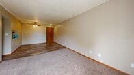 Located at 4320 Westbrook Dr in Ames, Iowa, this one-bedroom, one-bathroom unit offers a practical and well-organized single-floor layout. The living room serves as the heart of the home, featuring a mix of durable wood-look vinyl flooring and plush carpeting, warm neutral-toned walls, and a ceiling fan with light fixture. A sliding glass door fills the space with natural light and provides an outdoor view, enhancing the open feel of the room. The kitchen is efficiently designed with rich dark brown cabinetry, white countertops, a gas range with overhead ventilation hood, and matching wood-look flooring, creating a cohesive and functional cooking space. The bedroom offers comfortable carpeted floors, a ceiling fan, two windows that bring in ample natural light with views of surrounding greenery, and a set of double sliding closet doors providing generous storage. A connecting hallway links the main living areas to the full bathroom, which includes a clean, white tub and shower combination unit, a toilet, and wood-look flooring. Warm beige tones and wood-trimmed accents carry throughout the unit, contributing to a consistent and welcoming aesthetic throughout the entire space.