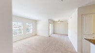 This single-floor residence offers a clean, light-filled layout designed for comfortable everyday living. The main living area is generously proportioned, featuring neutral wall tones, plush beige carpeting, and multiple windows dressed with horizontal blinds that invite an abundance of natural light. A ceiling fan with a light fixture serves the adjoining dining or secondary living zone, providing both ventilation and ambient lighting. A sliding glass door opens to an outdoor area, seamlessly connecting interior and exterior spaces.

The kitchen is thoughtfully designed with white raised-panel cabinetry extending to the ceiling, offering ample storage throughout. Rich, dark granite countertops provide a striking contrast against the white finishes, while recessed ceiling lights illuminate the workspace effectively. A peninsula with a matching granite surface adds additional prep space and a casual gathering point. White appliances, including a gas range with over-the-range microwave and a full-size refrigerator, are neatly integrated. Warm hardwood-style flooring grounds the kitchen space.

The bedroom area is carpeted and served by a ceiling fan, with convenient access to a spacious walk-in closet outfitted with extensive built-in shelving, hanging rods, and additional storage configurations. The overall palette throughout the unit is crisp and neutral, creating a bright, welcoming ambiance.
