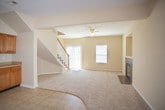 This two-story home offers a practical and comfortable layout spread across both levels. The main floor is anchored by a spacious living room featuring plush carpeting, a ceiling fan, and multiple windows that allow natural light to pour in, including a large sliding glass door. A wood-balustered staircase leads to the upper level. The entry foyer features neutral tile flooring and a paneled front door with a sidelight window.

The kitchen is well-appointed with warm wood cabinetry extending to the ceiling for generous storage, stainless steel appliances including a refrigerator, electric range, microwave, and dishwasher, complemented by ample countertop space and tile flooring.

Upstairs, the bedrooms are carpeted and equipped with ceiling fans. The primary bedroom features vaulted ceilings, natural light from multiple windows, and access to a walk-in closet with built-in shelving. Additional bedrooms offer ceiling fans and neutral carpeting throughout.

Two full bathrooms serve the home, each featuring a tub/shower combination, toilet, and tile flooring. The upper bath includes a vanity with wood cabinetry, while both maintain a clean, neutral aesthetic consistent with the rest of the home.
