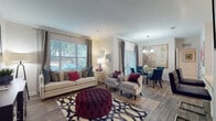 This single-floor residence offers a thoughtfully designed layout that balances comfort and style throughout. The open-concept living area is bathed in natural light streaming through large windows dressed with elegant drapes, highlighting the warm wood-look flooring underfoot and crisp crown molding above. A spacious seating arrangement anchors the room, complemented by a wall-mounted television and ample space for relaxing or entertaining.

Adjacent to the living area, the dining space features a glass-top round table beneath a modern chandelier, with direct access to an outdoor area via a glass-panel door. A large abstract artwork adds a sophisticated focal point to the corner.

The kitchen is well-equipped with white raised-panel cabinetry, granite countertops, stainless steel appliances including a range, microwave, dishwasher, and refrigerator, along with a peninsula that provides additional prep and dining space.

The bedroom is a serene retreat with plush carpeting, multiple windows offering outdoor views, and direct access to a spacious walk-in closet with built-in shelving and hanging storage. The bathroom features white cabinetry, granite countertops, an undermount sink, and wood-look flooring, completing this well-finished residence.