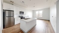 Located at 1184 Hank Aaron Dr in Atlanta, GA, this 1-bedroom, 1-bathroom unit offers a thoughtfully designed open-concept layout with clean, modern finishes throughout. The combined kitchen, dining, and living area serves as the heart of the home, centered around a large kitchen island with a built-in sink and light countertops. The kitchen is outfitted with stainless steel appliances — including a refrigerator, electric range, and built-in microwave — complemented by tall white cabinetry and track lighting overhead. Light hardwood-style flooring runs throughout the main living areas, contributing to a bright and airy atmosphere. A large window in the living area draws in natural light and frames open views of the surrounding Atlanta skyline and treetops below, indicating an elevated position within the building. The spacious bedroom features plush wall-to-wall carpeting and a generously sized window offering the same impressive city views. Two closets provide ample storage. The full bathroom includes a wide vanity with under-cabinet storage, a large mirror, and hardwood-style flooring. Additional utility and laundry spaces round out the functional layout, making this a well-equipped and efficiently organized living space.