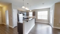 Located at 2000 Birchwood Circle in Bethlehem, Pennsylvania, this single-floor residence offers a thoughtfully designed open-concept layout that seamlessly connects the kitchen and living areas. The kitchen is a standout feature, showcasing dark espresso cabinetry, granite countertops, and a full suite of stainless steel appliances, including a refrigerator, microwave, and range. A peninsula with an overhanging granite countertop provides a casual dining or entertaining space, while three pendant lights suspended above add a stylish focal point. The living area benefits from generous natural light streaming through large, bright windows dressed with white blinds, creating an airy and welcoming atmosphere. The durable wood-look plank flooring runs throughout, lending warmth and continuity to the space. Neutral-toned walls complement the modern finishes, resulting in a clean, contemporary aesthetic. The layout is practical and efficient, making excellent use of the available space to create a comfortable, move-in-ready home in the Bethlehem, PA community.