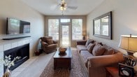 This single-floor residence offers a thoughtfully designed layout that balances comfort and functionality across its key living spaces. The living room serves as a welcoming focal point, featuring large windows with horizontal blinds that invite natural light, a ceiling fan, plush carpeting, and direct access to an outdoor patio through a glass-panel door — offering pleasant exterior views. The kitchen is outfitted with light wood cabinetry, ample counter space, tile flooring, and a full suite of white appliances including a refrigerator, range, dishwasher, and microwave. A dedicated dining area accommodates a round wooden table beneath an elegant chandelier, creating an inviting setting for meals. The primary bedroom is generously sized with carpet flooring, a ceiling fan, and a window with outdoor views, and connects to a spacious en-suite bathroom featuring a long vanity with dual sinks, light wood cabinetry, and wide mirrors. A second bedroom, equally comfortable with its own ceiling fan and natural light, is served by a well-appointed full bathroom with tile flooring, a vanity, and a shower. Neutral taupe wall tones and consistent finishes throughout lend the space a cohesive, understated elegance.