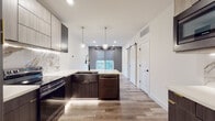 Located at 5655 Pershing in the Skinker-DeBaliviere neighborhood of St. Louis, Missouri, this thoughtfully designed single-floor residence showcases a contemporary aesthetic with high-end finishes throughout. The open-concept kitchen serves as the centerpiece of the space, featuring dark wood cabinetry complemented by a striking marble backsplash with gold veining, a waterfall-edge peninsula with white quartz countertops, and a deep farmhouse sink with a matte black faucet. Brass globe pendant lights hang overhead, adding a warm, modern touch, while luxury vinyl plank flooring in a natural wood tone extends throughout the entire unit. Black stainless steel appliances, including a French door refrigerator and dishwasher, complete the kitchen's refined look. A sliding barn door adds a stylish transitional element between spaces. The bedroom is bright and airy, with a large window offering neighborhood views, a ceiling fan, and direct access to the bathroom. The bathroom is a standout feature, boasting floor-to-ceiling marble-effect tile in the walk-in shower with black-framed glass doors, bold hexagonal floor tiles, a sleek wood-toned vanity with matte black hardware, and a framed mirror — a cohesive and elegant design that ties the entire unit together.