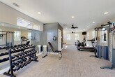 This fitness center offers a comprehensive workout environment spread across a single floor, thoughtfully designed to accommodate a wide range of exercise routines. The space is finished with neutral-toned carpet flooring and a clean white and gray color palette, creating a modern and motivating atmosphere throughout.

The main workout area is generously proportioned and benefits from abundant natural light streaming through multiple windows that frame outdoor views of the surrounding grounds. Recessed ceiling lighting and dual ceiling fans ensure the space remains well-lit and comfortable during any workout. The room houses a full lineup of cardio equipment, including treadmills, a stationary spin bike, and an elliptical machine, along with a multi-station cable machine for strength training. A dedicated free weights section features a tiered dumbbell rack with a full range of weights and an adjustable workout bench. A large wall-mounted mirror along one section amplifies the sense of space and supports proper form during training.

A separate studio-style room adjoins the main area, featuring vaulted ceilings, floor-to-ceiling mirrors, and ample open floor space, making it ideal for stretching, yoga, or group fitness activities. This room is also naturally lit with transom-style windows positioned high on the walls. Informational signage and amenity stations are thoughtfully placed near the entrance, completing this well-appointed fitness facility.