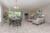 Located at 31275 Haggerty Rd in Novi, Michigan, this single-floor residence offers a thoughtfully designed layout with a warm, neutral palette throughout. The living room serves as the heart of the space, featuring plush carpeting, vaulted ceiling accents, and a sliding glass door that opens to a private balcony overlooking lush, tree-lined greenery — bringing abundant natural light into the room. A built-in shelving nook adds functional character to the living area.

The dining area, positioned adjacent to the living room, benefits from vaulted ceilings and its own sliding glass door to the balcony, creating an airy, open atmosphere ideal for entertaining. The kitchen is equipped with rich, warm-toned cabinetry, stone-look countertops, tile flooring, and stainless steel appliances, providing a practical and attractive workspace.

The primary bedroom features angled ceilings and plush carpeting, with a private en-suite bathroom appointed with dark wood cabinetry, stone countertops, and tile flooring. A second bedroom offers a bold green accent wall and natural light through a large window, served by a full bathroom with a shower-tub combination. The overall ambiance is comfortable and cohesive throughout.