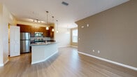 Located at 4101 Kenvil Dr in North Port, Florida, this single-floor residence offers a well-designed, open-concept layout that seamlessly connects the kitchen, dining, and living areas. Light wood-style flooring runs throughout the main living spaces, creating a clean and cohesive aesthetic, while warm neutral tones on the walls contribute to an inviting ambiance.

The kitchen is a functional highlight, featuring rich dark wood cabinetry, granite countertops, a curved breakfast bar peninsula with pendant lighting overhead, and a full suite of stainless steel appliances including a refrigerator, range, microwave, and dishwasher. A window above the sink brings in natural light. The open living and dining area is generously proportioned, with additional pendant lighting and a large window providing further brightness.

The bedrooms are finished with plush carpeting and painted in soft, neutral tones. Each room benefits from windows with blinds that allow natural light while maintaining privacy, and ceiling fans are present for added comfort. The bathroom is well-appointed with dark wood vanity cabinetry, granite countertops, and light wood-style flooring that mirrors the rest of the home. An entry area with access to a sliding glass door provides an easy connection to the outdoors.