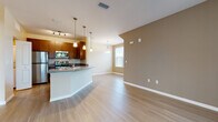 Located at 4101 Kenvil Dr in North Port, Florida, this single-floor residence offers a well-designed, open-concept layout that seamlessly connects the kitchen, dining, and living areas. Light wood-style flooring runs throughout the main living spaces, creating a clean and cohesive aesthetic, while warm neutral tones on the walls contribute to an inviting ambiance.

The kitchen is a functional highlight, featuring rich dark wood cabinetry, granite countertops, a curved breakfast bar peninsula with pendant lighting overhead, and a full suite of stainless steel appliances including a refrigerator, range, microwave, and dishwasher. A window above the sink brings in natural light. The open living and dining area is generously proportioned, with additional pendant lighting and a large window providing further brightness.

The bedrooms are finished with plush carpeting and painted in soft, neutral tones. Each room benefits from windows with blinds that allow natural light while maintaining privacy, and ceiling fans are present for added comfort. The bathroom is well-appointed with dark wood vanity cabinetry, granite countertops, and light wood-style flooring that mirrors the rest of the home. An entry area with access to a sliding glass door provides an easy connection to the outdoors.