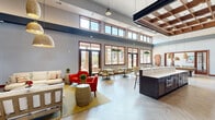 Located at 20200 Poplar Creek Pkwy in Brookfield, Wisconsin, this generously sized single-floor community space is thoughtfully designed to blend comfort, functionality, and modern style. The open-concept layout seamlessly connects a welcoming living area, a combined dining and kitchen zone, and recreational spaces, creating a versatile gathering environment throughout.

The living area is anchored by a striking floor-to-ceiling stacked stone fireplace, woven pendant lighting, and herringbone-patterned flooring that lends warmth and visual interest. Soaring ceilings with a distinctive wood-coffered canopy element over the kitchen bar add architectural drama. The kitchen and dining zone features a long bar with upholstered seating, sleek gray cabinetry, a mounted TV, and dark countertops, offering both a social and functional hub.

A separate dining area accommodates multiple seating arrangements and is outfitted with wall-mounted artwork and abundant natural light from large, wood-framed windows. A billiards table with pendant lighting occupies an additional recreational zone. Floor-to-ceiling windows and glass French doors open to an outdoor balcony, filling the interior with daylight and providing views of the surrounding community. Rich wood door framing and warm neutral tones complete the refined, inviting character of this space.