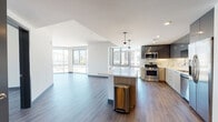 This single-floor residence showcases a thoughtfully designed open-concept layout with consistent wood-style flooring and crisp white walls throughout. The living area is generously proportioned, with floor-to-ceiling windows and sliding glass doors that invite abundant natural light and provide views of the surrounding neighborhood.

The kitchen is a standout feature, equipped with stainless steel appliances including a gas range, built-in microwave, refrigerator, and dishwasher. Dark upper cabinetry with a high-gloss finish contrasts with lighter wood-toned lower cabinets, while a marble-style backsplash adds visual interest. A large island with a white countertop and pendant lighting serves as both a functional workspace and a central gathering point.

The bedrooms are well-sized, each featuring large windows that bring in natural light and outdoor views. A hallway connects the private areas of the unit, with dark-paneled doors adding a refined accent.

Two bathrooms serve the residence. One features a soaking tub with tile surround, a vanity with wood cabinetry, and modern fixtures. The other offers both a soaking tub and a separate glass-enclosed shower, also finished with wood-toned tile and a white countertop vanity, delivering a clean, spa-like aesthetic.