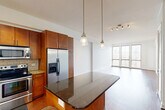 Located at 2800 Kirby Drive in Houston's desirable Upper Kirby neighborhood, this well-appointed one-bedroom, one-bathroom unit offers a thoughtfully designed layout across a single floor. The open-concept kitchen and living area serves as the heart of the home, featuring rich hardwood flooring, floor-to-ceiling windows fitted with wood blinds, and an abundance of natural light. The kitchen is equipped with stainless steel appliances, warm wood cabinetry, a subway tile backsplash, granite countertops, a center island with pendant lighting, and track lighting overhead — combining both style and functionality. The living area extends naturally from the kitchen, offering a spacious and versatile area with expansive views through large windows. The bedroom is a comfortable retreat finished with plush carpet, a ceiling fan with light fixture, and French doors that open onto a private balcony with outdoor views. A dedicated closet provides generous storage. The bathroom is well-appointed with tile flooring, a soaking tub with tile surround, and a separate glass-enclosed shower. Clean white walls throughout create a bright, cohesive aesthetic that complements the warm wood tones and natural finishes found across the unit.
