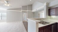 This single-floor residence offers a thoughtfully designed open-concept layout that seamlessly connects the main living areas. The living room is a standout space, featuring soaring vaulted ceilings, plush carpeting, a ceiling fan, a classic white-mantled fireplace, and a wide bank of windows that fill the room with natural light. A large wall mirror further enhances the sense of openness and brightness throughout.

The kitchen is well-equipped with rich dark wood cabinetry, light stone countertops, stainless steel appliances including a range, microwave, and dishwasher, and a peninsula with a double sink that opens to the living and dining areas — ideal for both cooking and entertaining. The hard surface flooring in the kitchen provides a practical contrast to the carpeted living spaces.

The bedrooms are generously proportioned, each featuring soft carpeting, ceiling fans, and windows that bring in natural light and outdoor views. The neutral gray tones used throughout the residence create a calm, cohesive aesthetic.

The bathrooms are finished with dark wood vanity cabinetry, white countertops, and a combination tub and shower. Additional storage is provided by overhead cabinetry. The consistent use of warm wood tones and neutral walls gives the entire residence a clean, modern, and welcoming character.