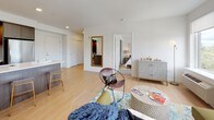 This well-appointed single-floor residence combines contemporary design with a bright, welcoming atmosphere throughout. The open-concept living area is anchored by light hardwood flooring and large windows that frame expansive outdoor views, flooding the space with natural light. A private balcony extends from the living room, enhancing the airy feel of the interior.

The kitchen is thoughtfully designed with dark wood cabinetry, stainless steel appliances including a gas range and refrigerator, and a generous white quartz peninsula with bar seating — ideal for casual dining or entertaining.

The living room offers ample space, with multiple windows providing cross-ventilation and sweeping neighborhood views. Two well-proportioned bedrooms feature plush carpeting and large windows. One bedroom offers direct balcony access and abundant natural light, while the other is a quiet, serene retreat with soft, neutral tones.

Both bathrooms are finished with modern dark wood vanities and clean white countertops. The primary bath features a double-sink vanity with tall cabinetry for generous storage, while the second bath is equally refined with hardwood-style flooring and contemporary fixtures. The overall aesthetic is clean, modern, and cohesive throughout.