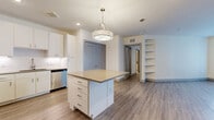 Located in Austin, TX 78757, this thoughtfully designed 2-bedroom, 1-bathroom residence offers a clean, modern aesthetic across a comfortable single-floor layout. The open-concept kitchen and living area serves as the heart of the home, anchored by a central island with a quartz-style countertop and ample drawer storage, illuminated by a stylish pendant light overhead. The kitchen is equipped with stainless steel appliances—including a French door refrigerator, range, and built-in microwave—complemented by crisp white cabinetry and a classic subway tile backsplash. Wood-look plank flooring runs throughout, adding warmth and continuity. Built-in shelving in the living area provides practical display and storage solutions. Both bedrooms are well-sized, filled with natural light from large windows with views of the surrounding community, and feature ceiling fans for comfort. The primary bedroom includes access to a walk-in closet with dual hanging rods and shelving. The bathroom showcases an L-shaped dual-sink vanity with warm tan countertops, white cabinetry, bold black-framed mirrors, and tile flooring. Additional storage is provided by two closets, including a mudroom-style entry with built-in hooks and cubbies.