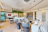 Located at 39 Railroad Ave in Haverhill, MA, this expansive single-floor amenity space spans a generous footprint across seven distinct areas, each thoughtfully designed to serve a specific purpose. The welcoming lobby greets visitors with large-format tile flooring, cove-lit ceilings, sculptural pendant lighting, and a built-in mailbox station topped with lush greenery. Adjacent to the entry is a bright coworking lounge featuring a bold geometric reception desk, suspended planter shelving, and long communal tables bathed in natural light from floor-to-ceiling windows. The main social lounge offers an open-plan layout with light hardwood flooring, a striking hanging garden installation, a wet bar with tiled backsplash, built-in shelving, and a fireplace — ideal for gathering and relaxation. A quieter media lounge provides a comfortable retreat with a wall-mounted television, slatted ceiling details, and plush seating. The fully equipped fitness center is divided into dedicated strength and cardio zones, featuring commercial-grade machines, floor-to-ceiling mirrors, and large windows with abundant natural light. A separate studio space accommodates group fitness activities. Completing the space is a spacious outdoor terrace with paved tile flooring, raised planters, and open views of the surrounding tree line — offering a serene setting for outdoor enjoyment.
