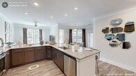 This well-appointed 2-bedroom, 2-bathroom single-story residence on Ellis Road in Durham, NC offers a thoughtfully designed open-concept layout. The kitchen is a standout feature, boasting dark espresso cabinetry, granite countertops, stainless steel appliances including a dishwasher and refrigerator, and a peninsula with bar seating — all flowing seamlessly into the dining and living areas. The living room is bathed in natural light from multiple windows dressed with elegant drapes, and features light hardwood-style flooring and crown molding throughout. The dining area is highlighted by large windows that invite abundant natural light. The generously sized primary bedroom includes plush carpeting, a ceiling fan, and a spacious walk-in closet with wire shelving systems offering ample storage. The second bedroom is equally comfortable, with carpeted floors, natural light, and a ceiling fan. Both bathrooms feature granite vanities with dark cabinetry and tile flooring. A dedicated laundry room with cabinetry adds everyday convenience. Crown molding, recessed lighting, and consistent finishes throughout give the home a polished, cohesive aesthetic.