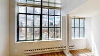 Located on North Broad Street in the heart of Philadelphia, this two-bedroom, two-bathroom bi-level residence is spread across two floors, offering a well-organized and functional layout. The main level features an open living area with soaring ceilings, warm hardwood-style flooring, and a striking staircase that connects to the upper level. Large, industrial-style grid windows flood the space with natural light and frame impressive panoramic views of the Philadelphia skyline.

The kitchen is well-appointed with rich cherry wood cabinetry, dark granite countertops, tile flooring, and a full suite of stainless steel appliances, including a refrigerator, dishwasher, microwave, and electric range. Two hallways provide efficient flow throughout both levels.

The generously sized primary bedroom features hardwood-style flooring and expansive windows with commanding city views. The second bedroom offers plush carpeting and a double closet. One bedroom also features access to a private balcony overlooking the cityscape. The two bathrooms include a tiled tub-shower combination and a separate glass-enclosed shower stall, both finished in neutral, clean tones. This residence combines urban convenience with comfortable, modern living in a prime Philadelphia location.