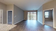 Located at 619 W Main St in Sun Prairie, Wisconsin, this single-floor unit offers a thoughtfully designed, open-concept layout with contemporary finishes throughout. The main living area features rich, dark wood-style flooring and neutral gray walls, creating a clean, modern aesthetic. A large sliding glass door with vertical blinds floods the space with natural light and provides direct access to an outdoor area with pleasant exterior views.

The kitchen is a standout feature, outfitted with high-gloss white cabinetry, granite countertops, and a full suite of stainless steel appliances including a gas range, microwave, refrigerator, and an undermount sink set into a central island with pendant lighting overhead. A gray subway tile backsplash adds a stylish accent.

The bathroom is well-appointed with a granite-topped vanity, an illuminated mirror, white cabinetry, and a tub-shower combination with wood-style flooring extending throughout. Bedrooms are carpeted and include access to a generously sized walk-in closet with built-in shelving and hanging rods. In-unit laundry is provided via a full-sized top-load washer and dryer with overhead shelving, adding practical convenience to this well-finished space.