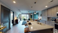Located at 417 W Peace St in Raleigh, NC, this single-floor residence delivers a refined urban living experience defined by modern architecture and thoughtful design details. The open-concept living and kitchen area serves as the heart of the home, where exposed concrete ceilings and light hardwood-style flooring establish an industrial-contemporary aesthetic. Large floor-to-ceiling windows flood the living space with natural light and frame views of the surrounding Raleigh cityscape and tree canopy, creating a seamless connection between interior and exterior. The kitchen is outfitted with wood-grain flat-front cabinetry, quartz countertops, stainless steel appliances, a tile backsplash, and a generous island with bar seating — ideal for both everyday living and entertaining. The living area accommodates a spacious seating arrangement beneath a ceiling fan mounted to the concrete soffit. The primary bedroom features a bold accent wall, exposed concrete ceiling, and direct access to a private balcony with outdoor views. An en-suite bathroom connects the bedroom corridor with a wood-tone vanity, quartz counters, and a glass-enclosed shower. A second bedroom provides a comfortable and well-lit retreat. Throughout, the design balances industrial structure with warm, contemporary finishes.