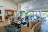 Located at 550 Paularino Ave in Costa Mesa, California, this single-floor community space is thoughtfully designed to blend comfort, functionality, and Southern California indoor-outdoor living. The open-plan layout connects the living, dining, and kitchen areas seamlessly, anchored by dramatic vaulted ceilings that lend a sense of grandeur and airiness throughout.

The living area is a standout, featuring a floor-to-ceiling stacked stone fireplace that serves as a bold architectural centerpiece. Warm hardwood-style flooring runs throughout, complementing the neutral palette of the walls and furnishings. A large wooden entertainment unit provides ample display and storage space, while lush indoor plants add natural vibrancy to the room.

The dining area is bathed in natural light, thanks to expansive floor-to-ceiling sliding glass doors that open directly to a resort-style outdoor pool area. This glass-wrapped space creates a seamless transition between indoors and outdoors, offering unobstructed views of the pool and surrounding landscaping.

The kitchen is well-appointed with warm wood cabinetry, granite countertops, stainless steel appliances, and a peninsula with bar seating. A window above the sink frames a pleasant view of the pool area, reinforcing the light-filled, open character of the space. Adjacent glass-walled offices are also visible, completing this versatile community hub.