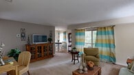 This thoughtfully designed single-floor residence offers a comfortable and functional layout across six distinct spaces, making efficient use of every square foot. The open-plan living and dining area serves as the heart of the home, featuring soft neutral-toned carpet, a textured ceiling, and large sliding glass doors that flood the space with natural light and provide access to a private balcony with outdoor views. The living area offers ample room for seating arrangements, while the adjacent dining space is lit by a stylish pendant light and framed by bright, striped curtains. The kitchen is fitted with warm wood cabinetry, granite countertops, a stainless steel sink, tile flooring, and includes a stacked washer and dryer unit — a practical convenience built directly into the space. The bedroom is a cozy retreat with carpeted floors, a window with natural light, and wall-mounted media provisions. A versatile office room features a window, carpet, and enough space to accommodate a loft-style workstation setup. The full bathroom is finished with tile flooring, a tub-shower combination, a granite-topped vanity with wood cabinetry, and tasteful framed wall art. A connecting hallway ties all rooms together seamlessly, completing this well-rounded, move-in-ready residence.