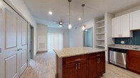This single-floor residence in Sunderland, Massachusetts offers a thoughtfully designed layout with modern finishes throughout. The kitchen serves as a central highlight, featuring a large island topped with granite countertops and rich cherry wood cabinetry paired with crisp white upper cabinets. A teal tile backsplash adds a distinctive accent, while stainless steel appliances—including a refrigerator, dishwasher, and microwave—complete the space. Pendant lighting hangs above the island, and light wood-style flooring extends throughout the main living areas. Built-in open shelving adjacent to the kitchen provides additional storage and display space, adding to the unit's functionality.

The open-concept layout connects the kitchen to the living area, which is equipped with a ceiling fan and access to a sliding glass door framed by vertical blinds, allowing natural light to filter in. The bedrooms feature plush carpeting, ceiling fans, and windows with blinds that bring in views of the surrounding landscape.

The bathrooms are finished with granite-topped vanities, wood cabinetry, and light hardwood-style flooring. One bathroom includes a shower-tub combination, while another provides direct access to a walk-in closet with wire shelving, offering practical storage solutions throughout the residence.