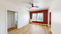 Located on N Alvarado Boulevard in the heart of Los Angeles, this single-floor unit blends classic architectural character with updated finishes throughout. The living area immediately draws attention with a striking exposed red brick accent wall framing a large window fitted with blinds, allowing natural light to filter in while offering views of the surrounding neighborhood. A ceiling fan overhead and light wood flooring underfoot contribute to the room's bright, airy feel.

The layout flows into a dedicated living space near the entry, also featuring a ceiling fan and the same warm wood flooring that runs consistently throughout the unit, creating a cohesive and clean aesthetic. The galley-style kitchen is efficiently designed with gray shaker-style cabinetry, stainless steel appliances including a gas range and full-size refrigerator, and a built-in range hood — offering a practical yet stylish cooking environment.

The bathroom is finished with floor-to-ceiling white subway tile surrounding a full soaking tub and shower combination. A mirrored medicine cabinet, a white vanity with under-cabinet storage, and a small window for ventilation and natural light complete the space. Overall, the unit presents a well-maintained, characterful living environment suited to urban Los Angeles living.