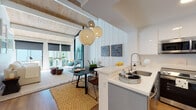 Located at 915 Shorepoint Ct in Alameda, CA, this single-floor residence blends coastal charm with contemporary design throughout its thoughtfully arranged layout. The open-plan living and dining area is a standout feature, characterized by striking exposed wood beam ceilings with light wood planking that lend warmth and architectural character to the space. Large floor-to-ceiling windows and sliding glass doors flood the area with natural light and provide direct access to an outdoor space, enhancing the airy, relaxed atmosphere. Woven pendant lights hang above the dining area, complementing the natural textures found throughout.

The kitchen is efficiently designed with white cabinetry, white quartz countertops, stainless steel appliances, and a peninsula that connects seamlessly to the dining area. Hardwood flooring runs through the main living spaces, adding continuity and warmth.

The bedroom features tall ceilings, carpeted flooring, and leads to a generously sized walk-in closet with built-in shelving. Two bathrooms serve the home: one with a clean, modern vanity and hardwood floors, and another with a full tub-shower combination. A separate room provides a quiet area suitable for a home office. Overall, the space presents a bright, cohesive coastal aesthetic.