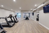 Located on Cedar St N in Kitchener, Ontario, this fitness facility offers a generously sized, single-floor gym designed to accommodate a full range of workout needs. The space features a clean, modern aesthetic with neutral-toned walls, light wood-style flooring, and recessed ceiling lighting throughout, creating a bright and welcoming environment conducive to exercise.

The main gym area is thoughtfully organized into distinct workout zones. A dedicated cardio section houses multiple treadmills and stationary cycling bikes, providing ample capacity for simultaneous users. A separate area accommodates several elliptical cross-trainers, offering low-impact cardiovascular options. Strength training is well-served by a multi-station cable and weight machine setup, suitable for a wide variety of resistance exercises.

Structural columns divide the open floor plan into natural activity zones without compromising the overall sense of spaciousness. The flooring throughout is easy-to-maintain and durable, appropriate for high-traffic fitness use. Decorative artwork is placed on the walls, adding a polished, finished quality to the space. A wall-mounted television screen is also present, enhancing the workout experience. Access points include a key-fob secured entry door, and safety signage is clearly posted. The overall design balances functionality with a clean, contemporary aesthetic.