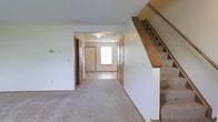 Located at 2332 Asics Dr. in Hilliard, Ohio, this two-story home offers a straightforward and functional layout across both levels. The main floor showcases a spacious, open carpeted living area with neutral wall tones that create a clean, understated atmosphere throughout. A carpeted staircase with a wooden handrail and banister leads to the upper level, positioned prominently along one wall and providing easy access between floors. The entryway area is well-defined, featuring a window that allows natural light to filter into the space, brightening the hallway and adjacent rooms. Multiple doors along the entry corridor suggest convenient access to closets or additional rooms, adding to the home's practical storage and spatial organization. The neutral carpet flooring flows consistently through the main living spaces, complementing the light-colored walls. Overhead lighting fixtures provide interior illumination throughout the hallways and entry areas. The overall ambiance of the home is simple and move-in ready, with a neutral palette that offers flexibility for personalization. The two-story configuration provides a clear separation between living and private spaces, making it a functional layout for everyday living in the Hilliard community.