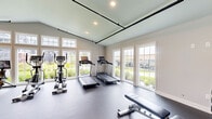 Located at 191 Spencer St in Manchester, CT, this fitness center is a thoughtfully designed single-room facility offering a comprehensive workout environment. The space features soaring vaulted ceilings that enhance the sense of openness, complemented by recessed lighting and sleek black overhead track hardware that add an industrial-modern aesthetic to the neutral, light-toned walls.

Natural light floods the room through an expansive array of large white-framed windows and glass doors, offering views of the surrounding green landscape and residential community. The durable rubber-speckled flooring provides both safety and comfort underfoot throughout the workout area.

The fitness center is well-appointed with a diverse selection of equipment. Cardio machines include multiple treadmills, ellipticals, and Echelon stationary bikes, all positioned to take advantage of the natural light and outdoor views. The strength training area features a multi-function cable machine, a full dumbbell rack with a variety of weights, a weight bench, a rowing machine, and resistance bands mounted along the wall. A large mirror enhances the strength training zone, while a stability ball and additional accessories round out the functional training options.

The space also includes practical amenities such as a waste bin and paper towel dispenser near the entrance, ensuring a clean and user-friendly environment for all fitness levels.
