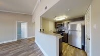 This single-floor residence is thoughtfully designed with a cohesive aesthetic that balances functionality and comfort throughout. The kitchen serves as a central highlight, featuring dark espresso cabinetry, granite-style countertops, a stainless steel refrigerator, electric range, and over-the-range microwave. A mosaic tile backsplash adds a decorative touch, while a peninsula with a built-in sink provides additional prep space and casual seating. Hardwood-style flooring flows through the kitchen and into the adjoining living areas, which benefit from crown molding, ceiling fans, and multiple windows dressed with blinds that invite natural light. The living space is generously proportioned, offering an open, versatile layout. Bedrooms are carpeted for added comfort, each equipped with a ceiling fan and window with natural views. The bathroom is finished with large-format, linear-patterned wall tile surrounding a full soaking tub and shower combination with chrome fixtures. Throughout the residence, neutral tones, consistent trim work, and quality finishes create a clean, modern atmosphere.