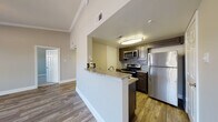 This single-floor residence is thoughtfully designed with a cohesive aesthetic that balances functionality and comfort throughout. The kitchen serves as a central highlight, featuring dark espresso cabinetry, granite-style countertops, a stainless steel refrigerator, electric range, and over-the-range microwave. A mosaic tile backsplash adds a decorative touch, while a peninsula with a built-in sink provides additional prep space and casual seating. Hardwood-style flooring flows through the kitchen and into the adjoining living areas, which benefit from crown molding, ceiling fans, and multiple windows dressed with blinds that invite natural light. The living space is generously proportioned, offering an open, versatile layout. Bedrooms are carpeted for added comfort, each equipped with a ceiling fan and window with natural views. The bathroom is finished with large-format, linear-patterned wall tile surrounding a full soaking tub and shower combination with chrome fixtures. Throughout the residence, neutral tones, consistent trim work, and quality finishes create a clean, modern atmosphere.