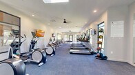 Located at 9425 20 Mile Rd in Parker, Colorado, this well-appointed fitness center offers a comprehensive exercise environment across a single, open floor. The space is designed with functionality and comfort in mind, featuring clean white walls, recessed lighting, and ceiling fans that maintain a bright and comfortable atmosphere throughout.

The exercise room is generously proportioned, accommodating an extensive lineup of cardio equipment including multiple treadmills, elliptical machines, stair climbers, and WaterRower rowing machines. A dedicated free weights area features a full dumbbell rack alongside adjustable workout benches, while a cable machine and stability balls round out the strength training options. Wall-mounted flat-screen TVs are positioned throughout the room for entertainment during workouts.

Large floor-to-ceiling windows and a skylight flood the interior with natural light and offer views of the surrounding greenery, creating an open and energizing environment. The flooring transitions between polished tile in the free weights zone and durable carpet in the cardio area, providing appropriate surfaces for each workout type. The layout flows logically from one exercise zone to the next, making efficient use of the available space. Overall, this fitness center delivers a clean, modern, and fully equipped facility suited for a wide range of fitness routines.