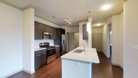 This well-appointed single-floor residence offers a thoughtfully designed layout that balances modern aesthetics with everyday functionality. The open-concept kitchen is a standout feature, showcasing dark espresso cabinetry with sleek hardware, light quartz countertops, and a full suite of stainless steel appliances including a gas range, microwave, and French door refrigerator. A large center island with an undermount sink and pendant lighting serves as both a prep space and casual gathering area, while rich hardwood-style flooring ties the kitchen seamlessly into the adjoining living area. The spacious living room is bathed in natural light from a sliding glass door that opens onto a private balcony, offering open views. A ceiling fan adds comfort to this generously sized room. The bedrooms are carpeted for warmth and comfort, each featuring a ceiling fan and window for natural light. The bathrooms are finished with dark cabinetry, wood-style flooring, and tub-shower combinations, with one bathroom providing direct access to a walk-in closet with built-in shelving. A dedicated laundry area houses a full-size top-loading washer and dryer, adding convenience to this well-rounded residence.