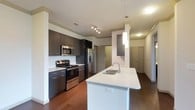 This well-appointed single-floor residence offers a thoughtfully designed layout that balances modern aesthetics with everyday functionality. The open-concept kitchen is a standout feature, showcasing dark espresso cabinetry with sleek hardware, light quartz countertops, and a full suite of stainless steel appliances including a gas range, microwave, and French door refrigerator. A large center island with an undermount sink and pendant lighting serves as both a prep space and casual gathering area, while rich hardwood-style flooring ties the kitchen seamlessly into the adjoining living area. The spacious living room is bathed in natural light from a sliding glass door that opens onto a private balcony, offering open views. A ceiling fan adds comfort to this generously sized room. The bedrooms are carpeted for warmth and comfort, each featuring a ceiling fan and window for natural light. The bathrooms are finished with dark cabinetry, wood-style flooring, and tub-shower combinations, with one bathroom providing direct access to a walk-in closet with built-in shelving. A dedicated laundry area houses a full-size top-loading washer and dryer, adding convenience to this well-rounded residence.