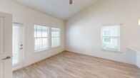 Located at 9000 Little Palm Way in Venice, FL, this two-story home offers a well-designed layout across two floors, with the main living areas on the ground level and additional bedrooms above. The open-concept main floor is anchored by a bright, airy living and dining area featuring soaring vaulted ceilings and recessed lighting that amplify the sense of space. The contemporary kitchen is outfitted with white shaker cabinetry, a gray tile backsplash, stainless steel appliances including a side-by-side refrigerator, electric range, and built-in microwave, along with a peninsula sink that seamlessly connects to the living area. Light wood-look flooring flows throughout, lending a clean, cohesive aesthetic. Each of the three bedrooms is well-proportioned, featuring ceiling fans, natural light from multiple windows, and easy access to closet space. The three bathrooms are finished in a neutral palette, with one featuring a tiled tub-surround and white vanity with brushed nickel fixtures. A dedicated laundry room houses a full-size washer and dryer. The exterior features a fully fenced, private backyard with a white vinyl privacy fence and a small lawn area, ideal for outdoor enjoyment. A utility room and ample hallway space add further practicality to this move-in-ready home.