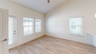 Located at 9000 Little Palm Way in Venice, FL, this two-story home offers a well-designed layout across two floors, with the main living areas on the ground level and additional bedrooms above. The open-concept main floor is anchored by a bright, airy living and dining area featuring soaring vaulted ceilings and recessed lighting that amplify the sense of space. The contemporary kitchen is outfitted with white shaker cabinetry, a gray tile backsplash, stainless steel appliances including a side-by-side refrigerator, electric range, and built-in microwave, along with a peninsula sink that seamlessly connects to the living area. Light wood-look flooring flows throughout, lending a clean, cohesive aesthetic. Each of the three bedrooms is well-proportioned, featuring ceiling fans, natural light from multiple windows, and easy access to closet space. The three bathrooms are finished in a neutral palette, with one featuring a tiled tub-surround and white vanity with brushed nickel fixtures. A dedicated laundry room houses a full-size washer and dryer. The exterior features a fully fenced, private backyard with a white vinyl privacy fence and a small lawn area, ideal for outdoor enjoyment. A utility room and ample hallway space add further practicality to this move-in-ready home.