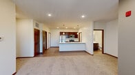 Located at 9941 S 37th St in Lincoln, Nebraska, this thoughtfully designed 2-bedroom, 2-bathroom residence offers a comfortable and functional single-floor layout. The open-concept living and kitchen area serves as the heart of the home, where light wood-look flooring transitions seamlessly into plush carpeting in the living room. The kitchen is a standout feature, equipped with rich dark-wood cabinetry, stainless steel appliances including a refrigerator, range, and microwave, and a generously sized island with a white quartz countertop, double sink, and pendant lighting overhead. Recessed lighting throughout enhances the bright, clean atmosphere. The living room extends toward a sliding door with vertical blinds, allowing for natural light and outdoor access. Both bedrooms are carpeted and feature ceiling fans, vertical blinds, and easy access to closets. The primary bedroom includes its own dedicated bathroom with dark cabinetry and a white countertop vanity. A second full bathroom serves the rest of the home. A dedicated in-unit laundry room houses a full-size washer and dryer with overhead shelving. Three closets provide ample storage throughout, and a hallway connects the private spaces efficiently. Warm wood door trim adds a cohesive, polished finish throughout the residence.