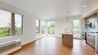 This well-designed 3-bedroom, 2-bathroom unit offers a thoughtful single-floor layout that maximizes both functionality and comfort. The open-concept kitchen and living area serves as the heart of the home, featuring warm wood-toned cabinetry, a sleek island with a built-in sink and pendant lighting above, a herringbone tile backsplash, and stainless steel appliances. Large floor-to-ceiling windows flood the space with natural light and frame lush, tree-lined views, creating a bright and airy atmosphere throughout. Hardwood-style flooring runs continuously through every room, adding warmth and cohesion to the clean, modern aesthetic defined by crisp white walls and contemporary finishes. The three bedrooms are generously proportioned, with the primary bedroom offering notable space and serene outdoor views. A dedicated closet provides convenient storage. The two bathrooms are finished in a modern style — one featuring a full soaking tub with shower and chrome fixtures, and the other a glass-enclosed walk-in shower alongside a wood-paneled vanity with ample drawer storage. An in-unit washer and dryer adds everyday convenience. The overall ambiance is clean, bright, and contemporary, ideal for comfortable modern living.