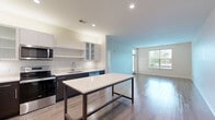 Located at 6201 Johnson Dr, Unit 306 in Mission, Kansas, this one-bedroom, two-bathroom residence offers a well-designed single-floor layout with a thoughtful blend of modern finishes and functional living spaces. The open-concept kitchen and living area serves as the heart of the home, featuring rich wood-toned lower cabinetry paired with white upper cabinets with glass-front accents, light quartz countertops, a central island, and a full suite of stainless steel appliances including a refrigerator, range, microwave, and dishwasher. The living area is bathed in natural light through large windows and is finished with smooth hardwood-style flooring that extends throughout the main areas. The bedroom is a comfortable retreat with plush carpeting, a ceiling fan, and a bright window overlooking the outdoors. The primary bathroom is generously appointed with a dual-sink vanity featuring dark cabinetry, tile flooring, a large mirror, and a tiled walk-in shower. A second bathroom provides a convenient water closet with wood-style flooring. Completing the home is a dedicated laundry room equipped with a full-size Whirlpool washer and dryer and built-in shelving above for additional storage.