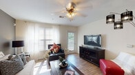 Located on October Road in Clarksville, Tennessee, this single-story residence offers a well-organized layout designed for comfortable everyday living. The floor plan, visible in the 3D overview, reveals a thoughtful arrangement of living, sleeping, kitchen, and bathroom spaces that flow naturally from one area to the next.

The living room serves as the heart of the home, featuring wood-look flooring, abundant natural light from multiple windows dressed with sheer curtains and blinds, and a ceiling fan with light fixture overhead. A glass door leads directly to a private balcony, extending the living space outdoors and enhancing the sense of openness. An accent wall in a deeper gray tone adds visual depth to the room.

The galley-style kitchen is lined on both sides with light wood cabinetry and ample counter space, providing efficient storage and workspace. White appliances, including a refrigerator, range, microwave, and dishwasher, are cleanly integrated throughout. Wood-look flooring continues here, maintaining a cohesive aesthetic.

The bedrooms are carpeted and well-proportioned, each accommodating a full-sized bed with room to spare. Natural light filters in through large windows with sheer coverings. The bathroom features wood-look flooring, a curved shower rod, a tub-shower combination, and a vanity with light wood cabinetry and warm countertops, completing the home's functional and inviting character.