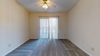 This single-floor unit offers a practical and functional layout across several well-defined spaces. The main living area is generously sized, featuring plush gray carpeting, neutral-toned walls, and a textured ceiling. A ceiling fan with an integrated light fixture provides both ventilation and ambient lighting. A wide sliding glass door, dressed with vertical blinds, fills the room with natural light and provides direct access to an outdoor area. The transition between the carpeted living space and tile flooring near the entryway is clearly defined.

A secondary carpeted room mirrors the living area's design, complete with its own ceiling fan and a window fitted with horizontal blinds, allowing for natural light while maintaining privacy.

The kitchen features light-toned laminate countertops and wood-trimmed cabinetry with cream-colored panels. White appliances, including a refrigerator, electric range, and over-the-range microwave, are neatly integrated into the layout. Light tile flooring runs throughout the kitchen and connects to adjacent spaces.

The bathroom offers a full tub-shower combination with tile surround, a toilet, and an extended vanity with ample under-sink storage. A wide mirror spans the length of the vanity, complemented by a multi-bulb light fixture above, creating a bright and practical space.