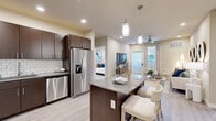 This single-floor residence in Vallejo, California offers a well-designed, open-concept layout with modern finishes throughout. The kitchen serves as a central hub, featuring dark espresso cabinetry, a white subway tile backsplash, stainless steel appliances including a French door refrigerator, dishwasher, and range, along with a large island with quartz-style countertops and pendant lighting overhead. Light wood-style flooring flows seamlessly from the kitchen into the living and dining areas.

The living room is bright and welcoming, with recessed lighting, a ceiling fan, and a glass door that invites natural light while providing outdoor access. The space connects smoothly to a dedicated media area and dining space, creating a cohesive and functional layout.

The bedrooms are carpeted for comfort and feature ceiling fans, ample natural light from large windows with blinds, and neutral wall tones. The bathrooms are well-appointed with dark wood vanities, gray countertops, undermount sinks, and a combination tub and shower. An in-unit stacked washer and dryer is conveniently located within the unit. Overall, the space presents a clean, contemporary aesthetic with practical, high-quality finishes.